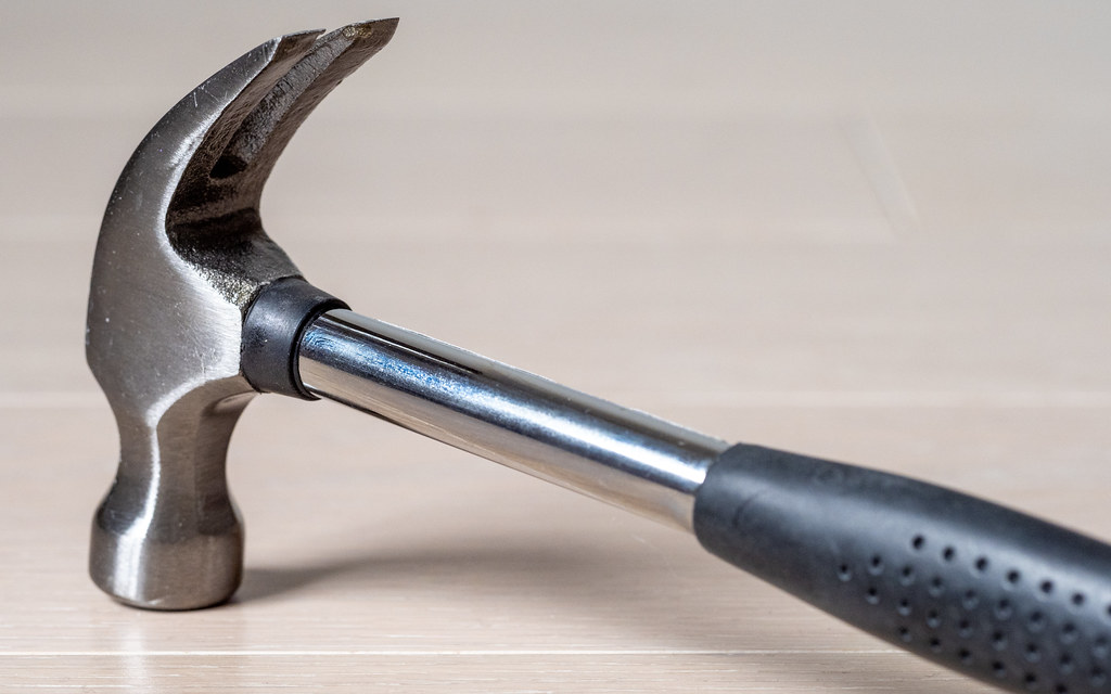 Metal hammer with black rubber handle on a piece of wood.