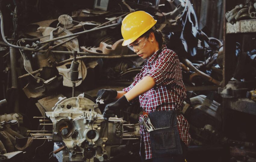 woman wears yellow hard hat holding vehicle part