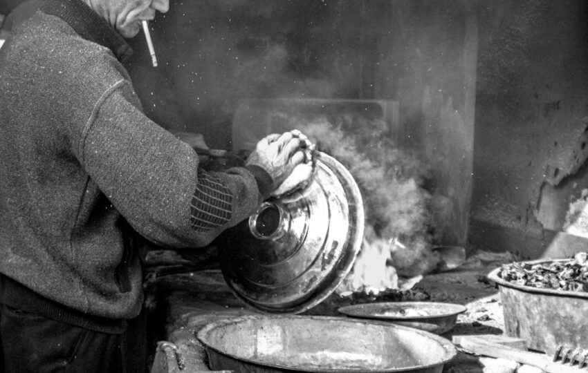 a grayscale of a man washing a stainless steel lid while smoking a cigarette